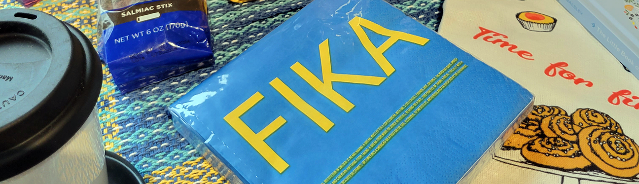 A coffee cup, a pack of Fika napkins, a bag labeled Salmiac Stix, and an illustrated napkin with cinnamon rolls and Time for fika text are on a textured surface.