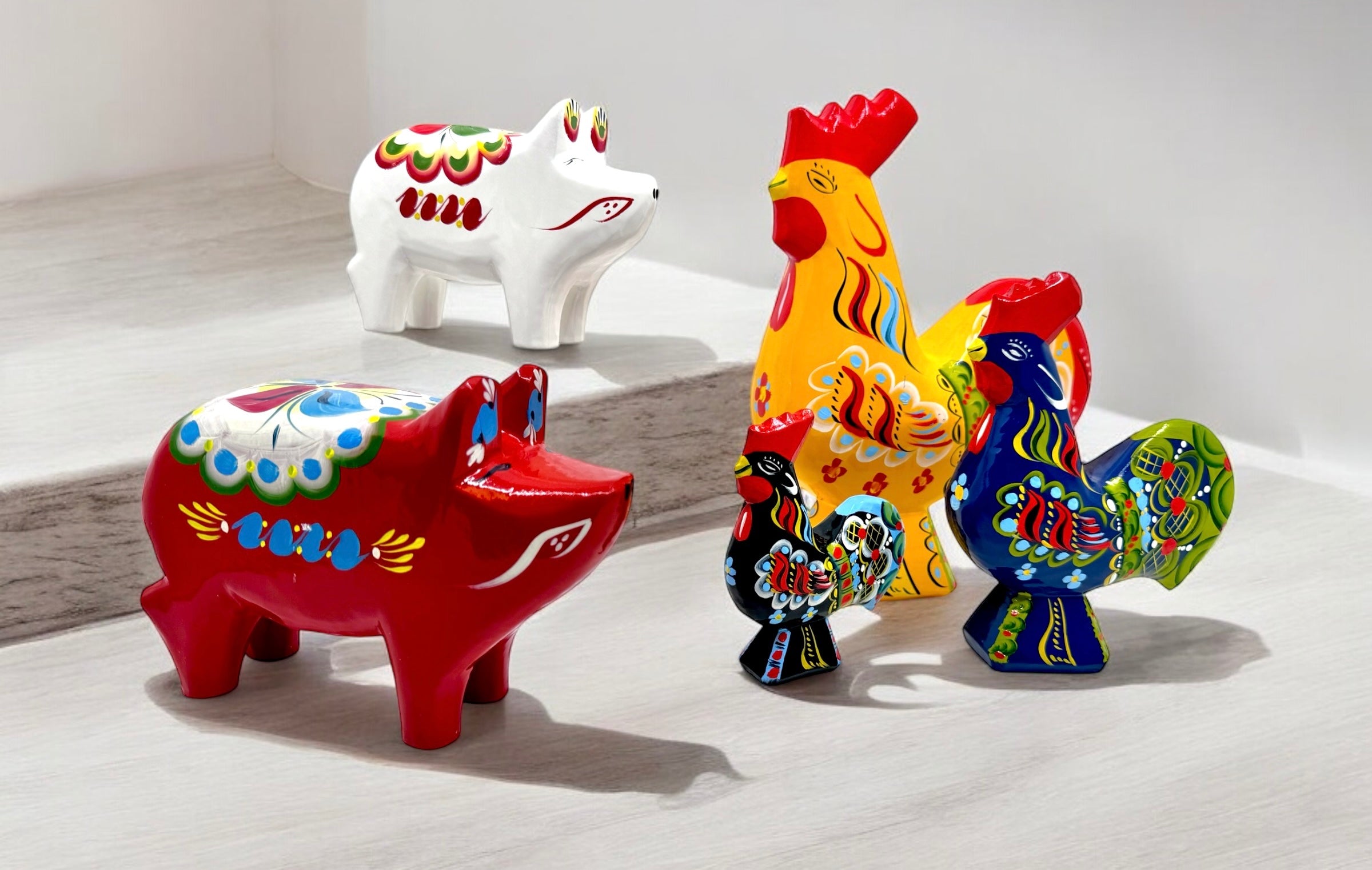 Colorful ceramic figurines of a red pig, a white pig, and three roosters in various colors with decorative patterns, arranged on a tiled surface.