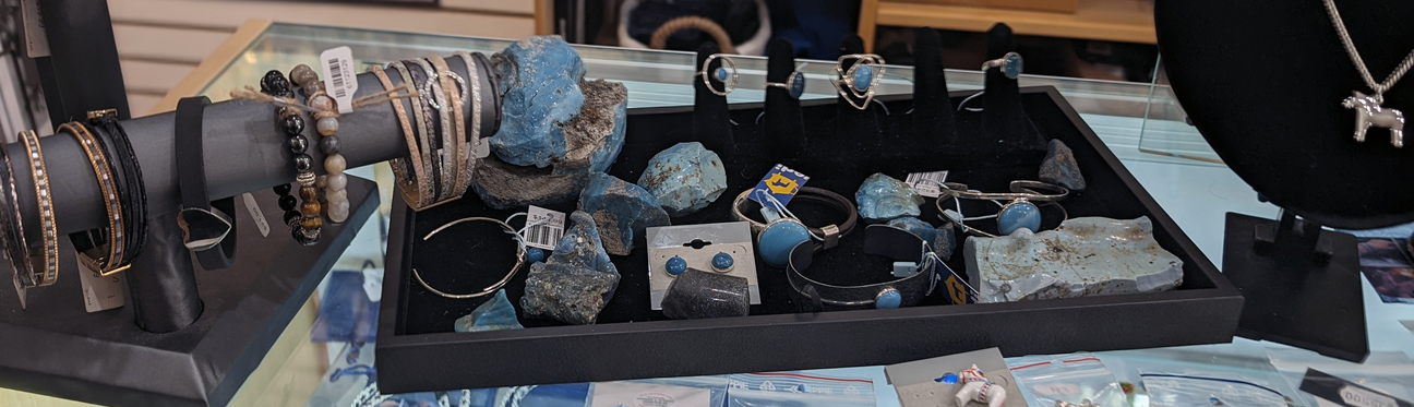 Jewelry display featuring bracelets, rings, earrings, and necklaces with blue stones on a black and glass counter.