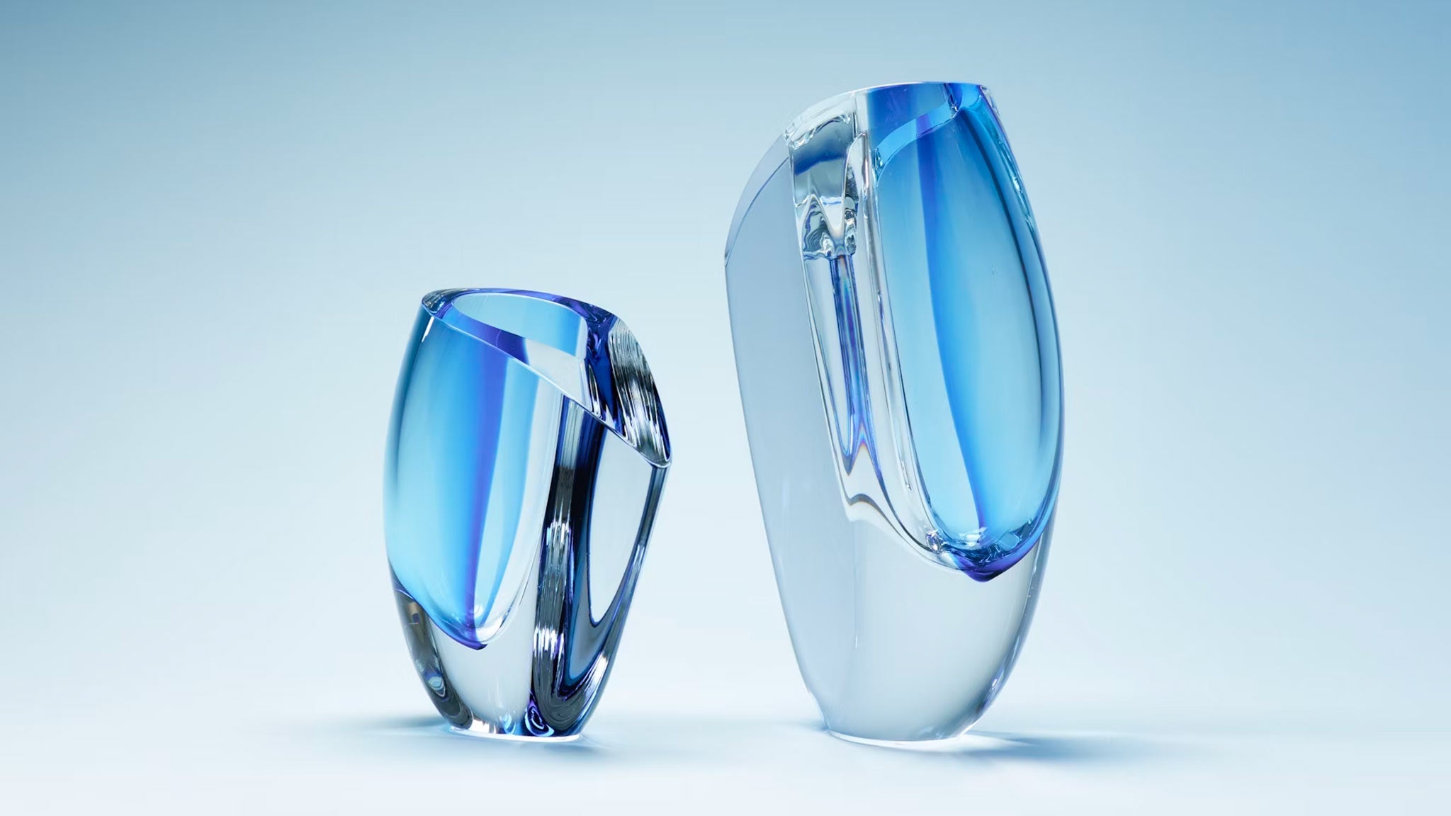 Two clear, asymmetrical glass sculptures with blue tint against a light blue background.