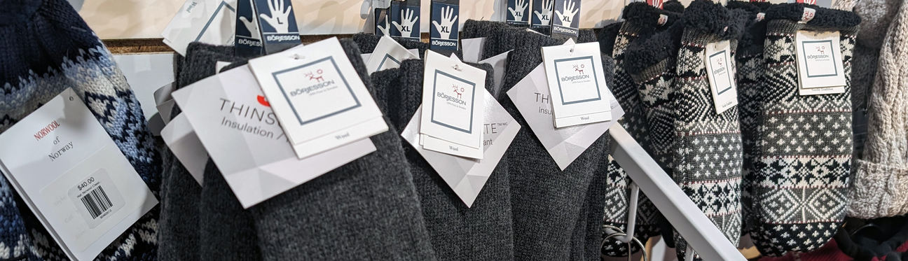 Close-up of various knitted winter socks with different patterns and colors displayed on a rack, each with a price tag and label.