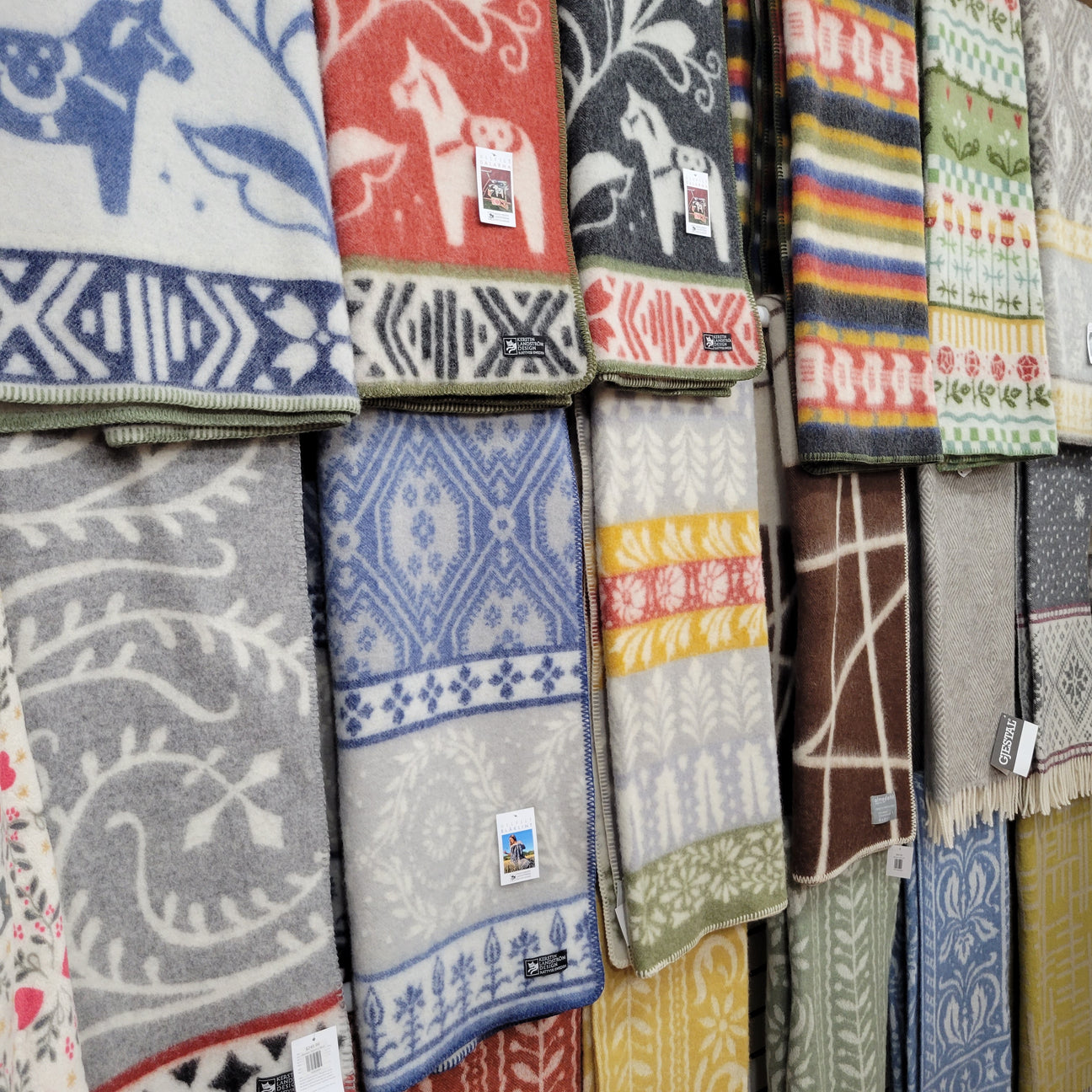A display of colorful wool blankets with various patterns, including animals, flowers, and abstract designs, hanging on a wall.