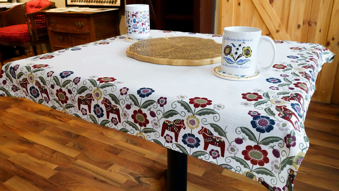 Table with a floral-patterned cloth, two coffee mugs, and a woven mat at the center, on a wooden floor.