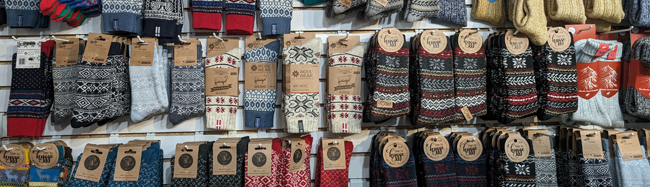 A display of colorful, patterned woolen socks and mittens hangs on a wall, each with a brown label.