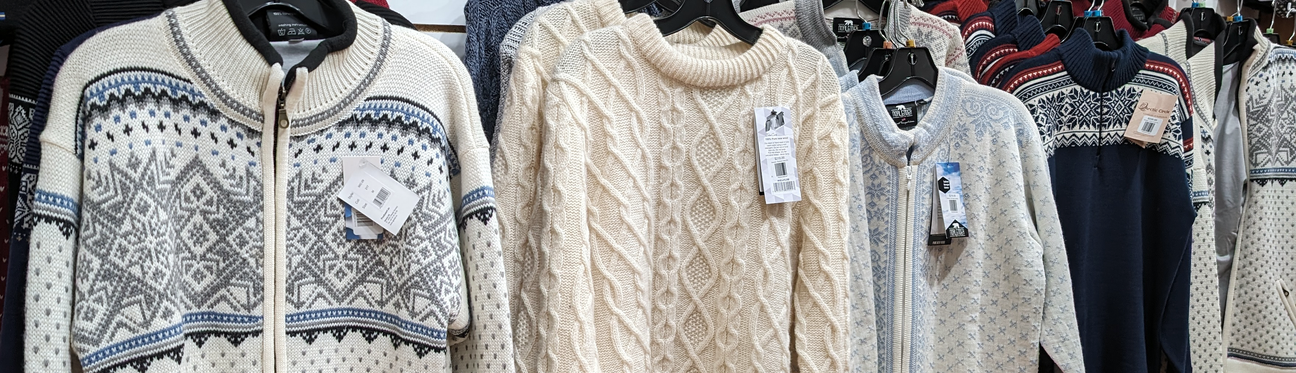 A row of winter sweaters displayed on hangers, featuring various patterns and colors including cream cable knit and geometric designs.