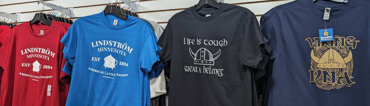 A selection of T-shirts on hangers, featuring designs related to Lindström, Minnesota, with text about Vikings and helmets.