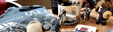 An assortment of Viking-themed items including mugs, a shirt, figurines, a coaster, and a small wooden ship displayed on a table.