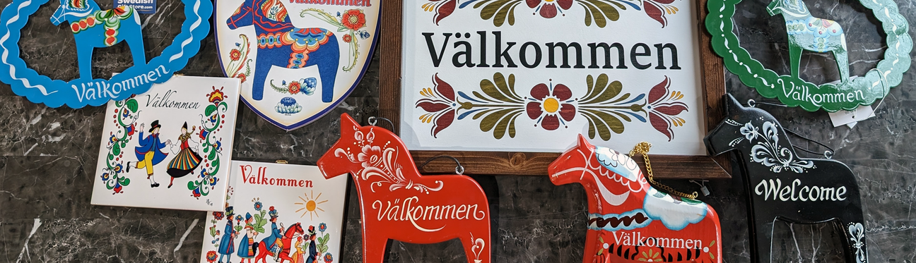 Various signs and decorations with Välkommen (Welcome) displayed in different styles and colors, including images of traditional Swedish Dala horses.