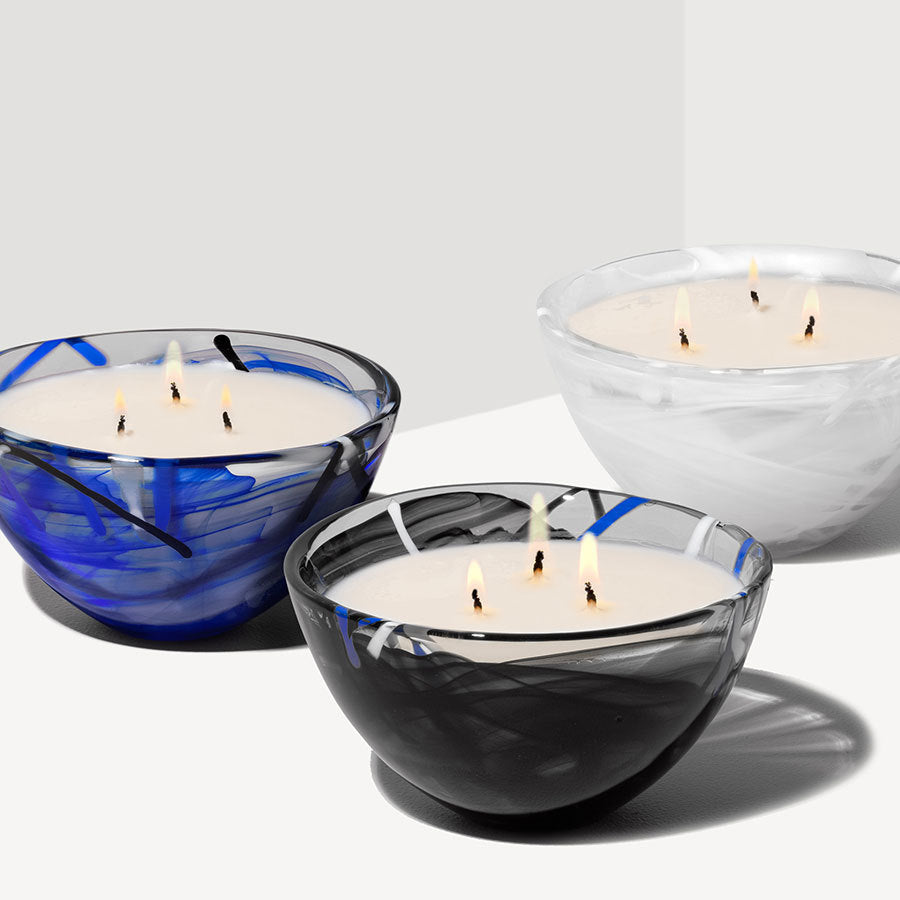 Three decorative candles are in glass bowls with swirling patterns: one blue, one black, and one white. Each candle has multiple lit wicks.