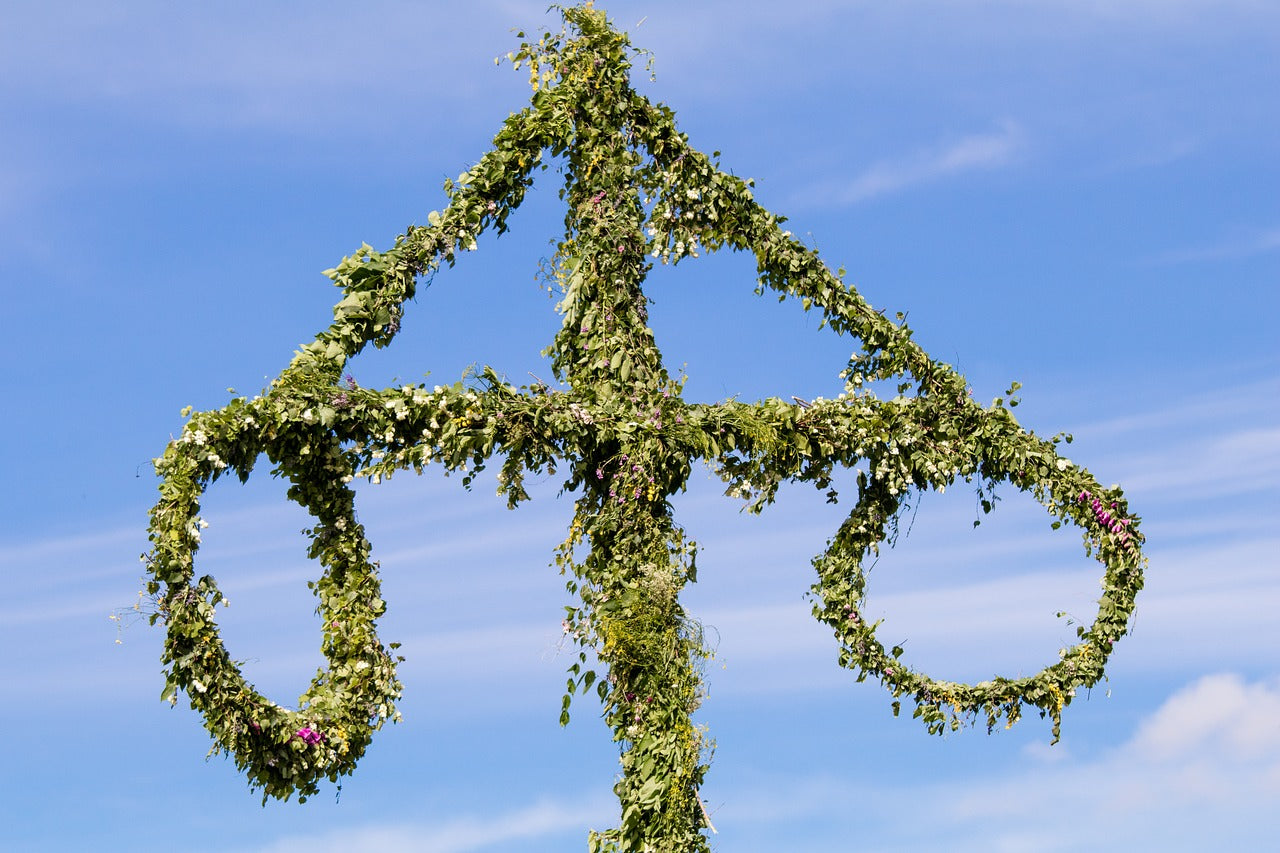 A traditional Swedish maypole decorated with green leaves and flowers stands against a bright blue sky, symbolizing Midsummer celebrations.