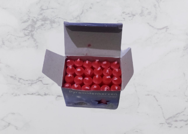 Open box of a 24-pack of Candles: Christmas Pyramid Candles, vibrant red and elegantly pyramid-shaped, resting on a marble surface.