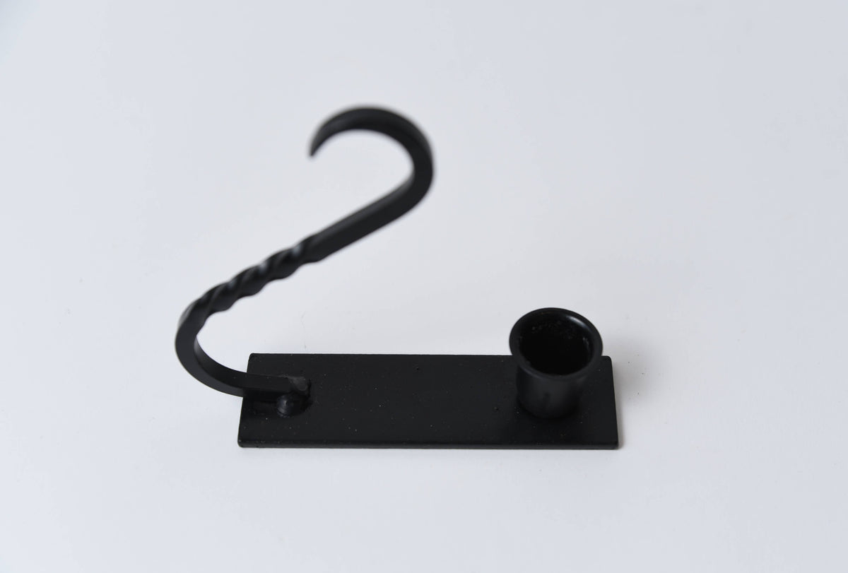 Iron taper holder with a flat base, cylindrical candle cup, and a curved, twisted handle.