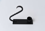 Iron taper holder with a flat base, cylindrical candle cup, and a curved, twisted handle.