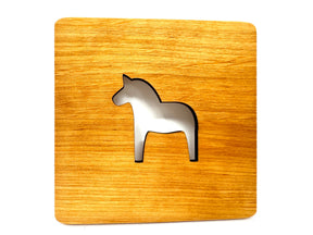 A charming square coaster, laser cut from alder wood, features a silver Swedish Dala Horse silhouette at its center.