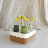 The Candle Holder: Mini Vases for Stumpastaken Candleholder 2-pack holds two green candles and three mini vases with yellow daffodils, beautifully arranged on a white and cork base against soft beige fabric for an elegant table display.