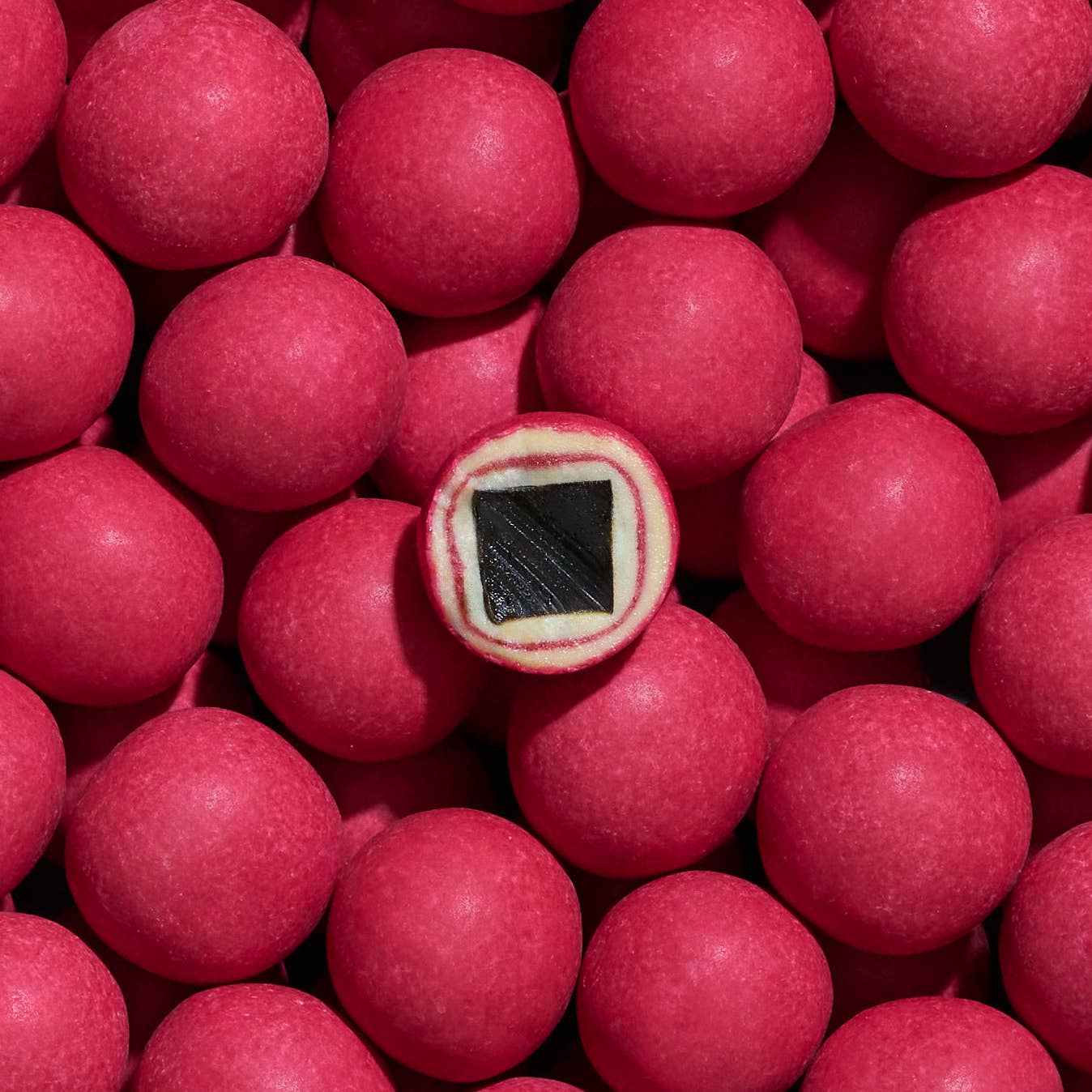 A group of round, pink Lakrids: Crispy Raspberry Danish Gourmet Licorice candies (Limited Edition, 4.41 oz), with one cut open to show a black licorice center and a white layer.