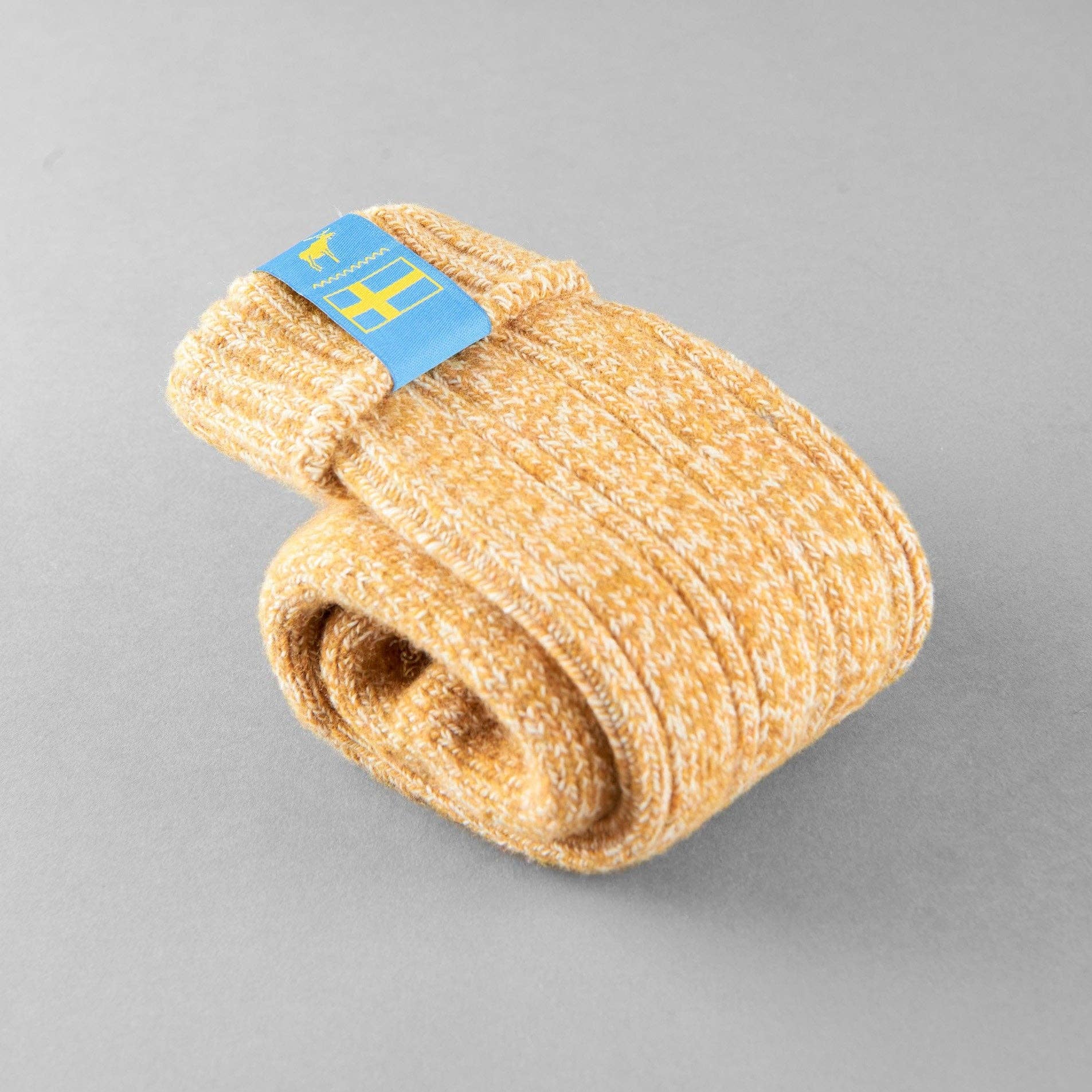 A rolled-up pair of yellow unisex Swedish Lagom socks with a blue tag displaying a Swedish flag, made from a wool blend, positioned on a gray background.