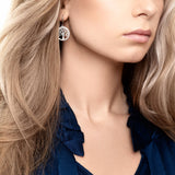 Woman with long blonde hair wears a navy blouse and showcases Tree of Life in Sterling Silver with Beautiful Luster earrings, photographed from the shoulders up with focus on the jewelry.