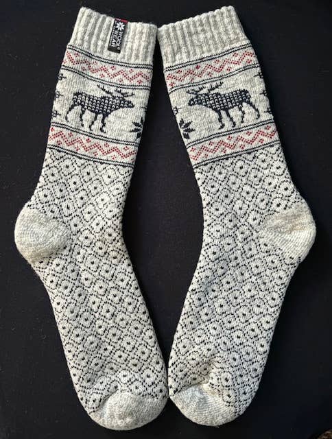 Beige wool socks with black Nordic patterns and reindeer motifs, displayed flat on a black background.