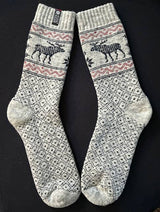 Beige wool socks with black Nordic patterns and reindeer motifs, displayed flat on a black background.