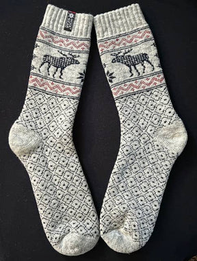 Beige wool socks with black Nordic patterns and reindeer motifs, displayed flat on a black background.