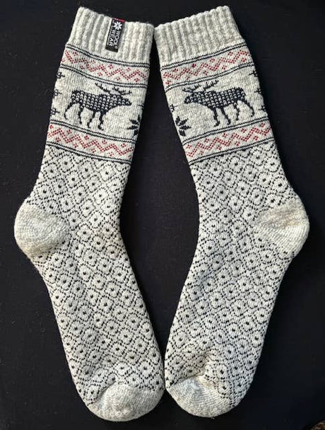 Beige wool socks with black Nordic patterns and reindeer motifs, displayed flat on a black background.