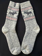 Beige wool socks with black Nordic patterns and reindeer motifs, displayed flat on a black background.