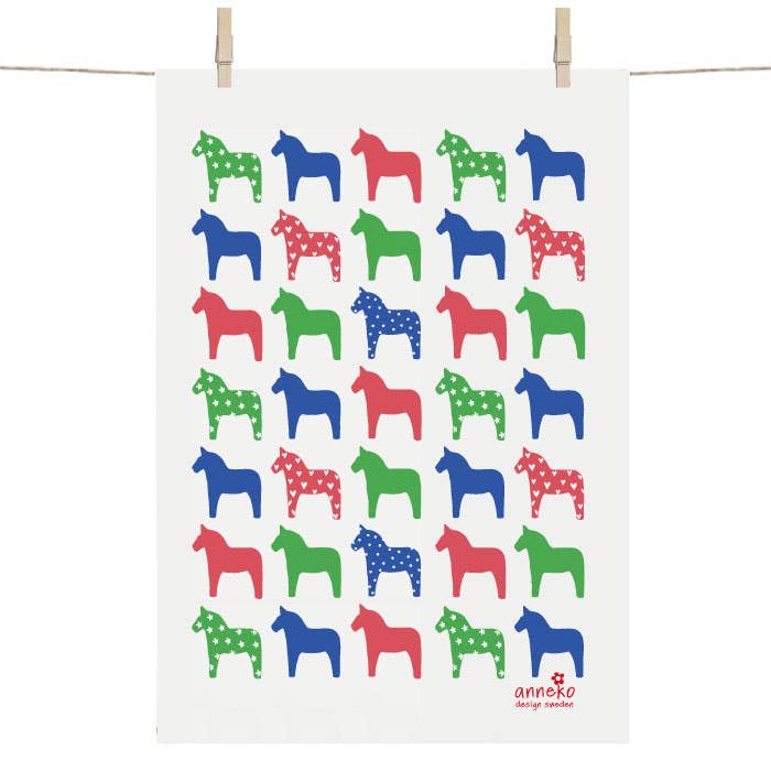 Tea towel called "Dalahäst Classic" showcasing a pattern of green, red, and blue horse silhouettes with some polka-dotted details, designed by Anneli Asplund for Anneko Design Sweden.