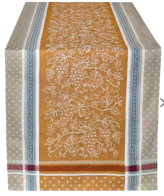 Cotton table runner with a mustard-yellow center featuring white grapevines, flanked by beige and blue geometric borders.