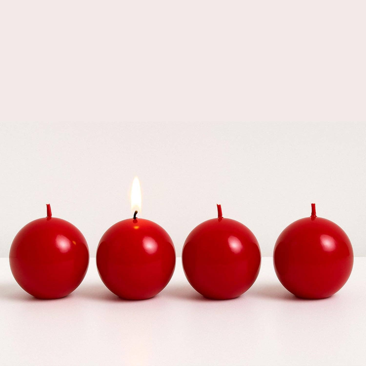 Four Cranberry Red Ball Candles, 2.5" diameter, are arranged in a row with only the second candle lit, while the others remain unlit for a charming decorative display.