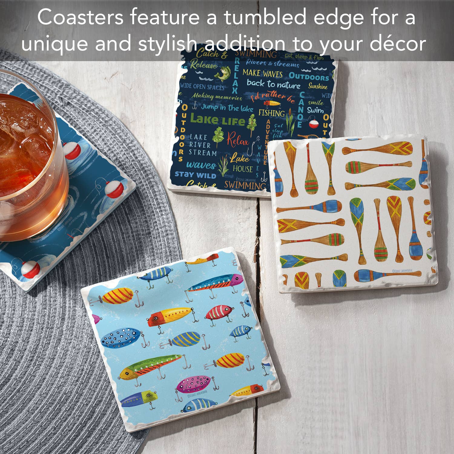 Three "Lake Living Coaster #1" pieces with vibrant square designs, showcasing fish, oars, and nautical phrases, rest on a wooden table. Each coaster is crafted from absorbent stone with a cork backing, exuding a rustic charm while one supports a drink.