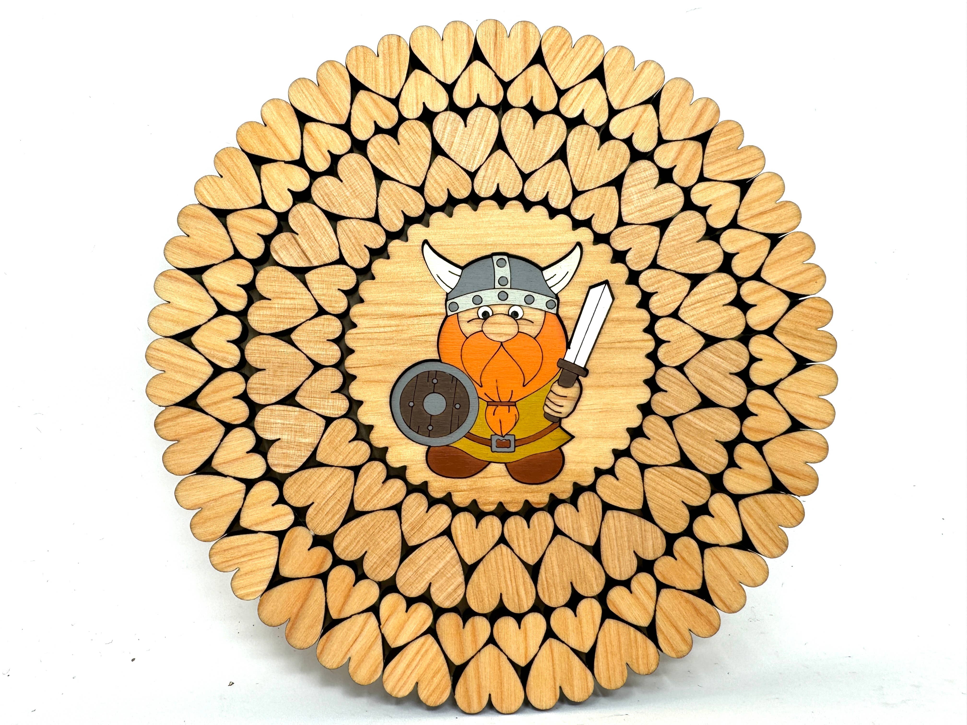 Handmade in Estonia, this wooden trivet features laser-cut heart pieces and showcases a cartoon Viking with an orange beard, holding a sword and shield at the center.