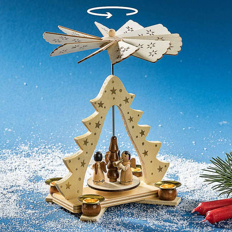 The Marketplace24 Pyramid: Christmas Pyramid Candle Holder with Angels, Made in Germany and standing 8" tall, features charming angel figures, a tree centerpiece, candle holders with red candles, and a spinning propeller top indicated by an arrow showing its movement. Set against a blue snowy background with pine branches, this traditional German holiday decor piece adds festive beauty to your home.