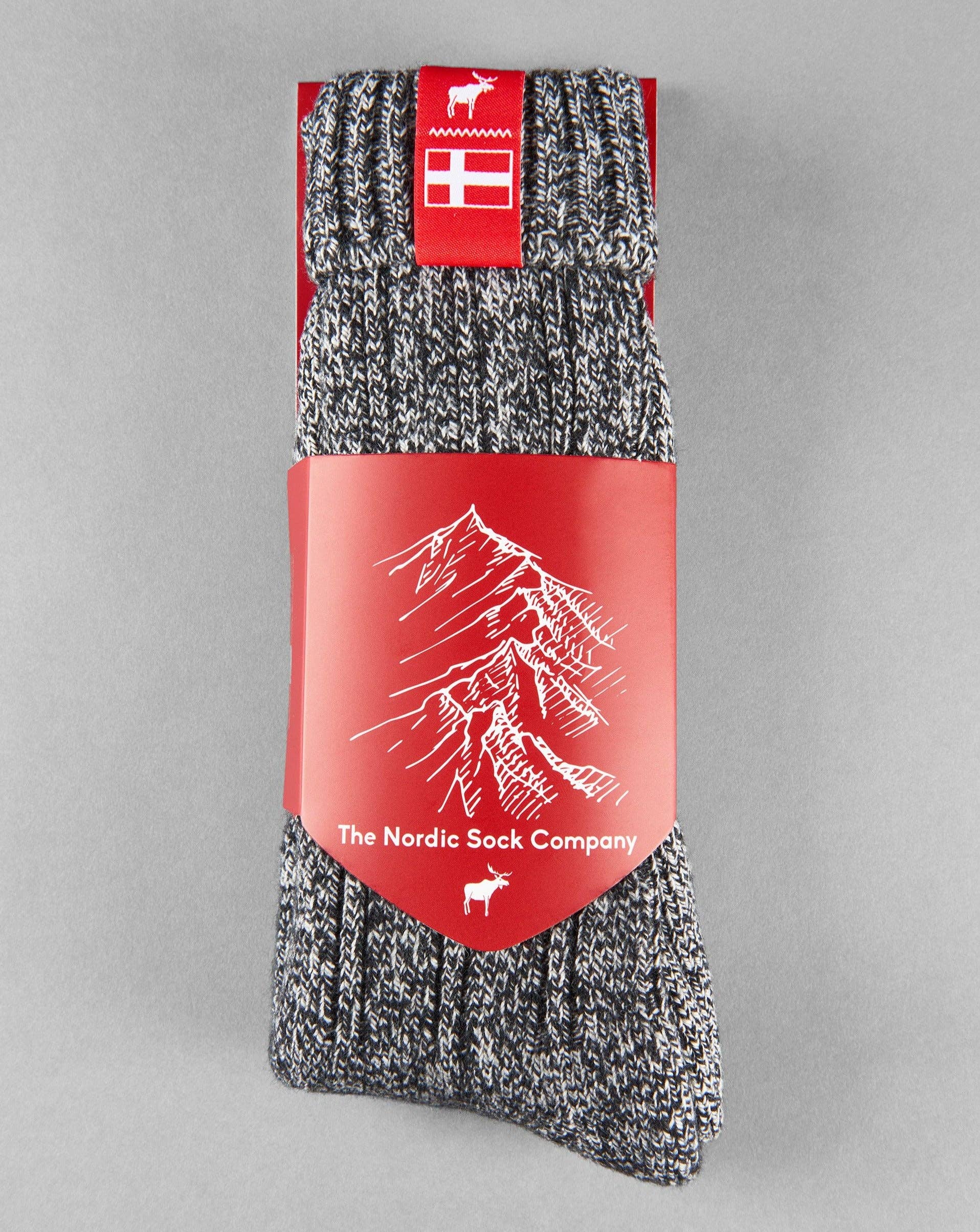 Introducing the Nordic Noir Danish Hygge Socks, a stylish pair in gray and black with a red label that features a white mountain graphic and The Nordic Sock Company branding—ideal for wrapping your feet in cozy warmth this winter.