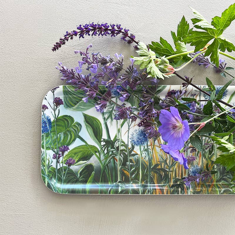 A Koustrupco Anne Just birch veneer tray (32x15 cm) showcases beautiful blue and purple flowers, accented by additional botanical patterns on a light gray background.