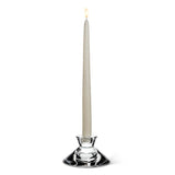 A lit white taper candle elegantly adorns the Reversible Glass Candleholder (4.5" D) against a white background, casting versatile candlelight suitable for any occasion.