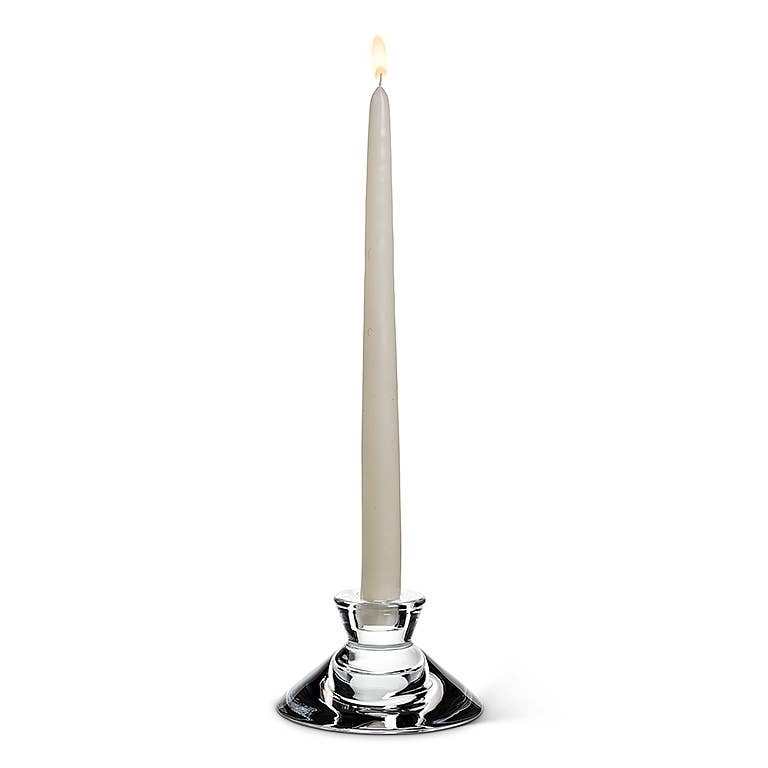 A lit white taper candle elegantly adorns the Reversible Glass Candleholder (4.5" D) against a white background, casting versatile candlelight suitable for any occasion.