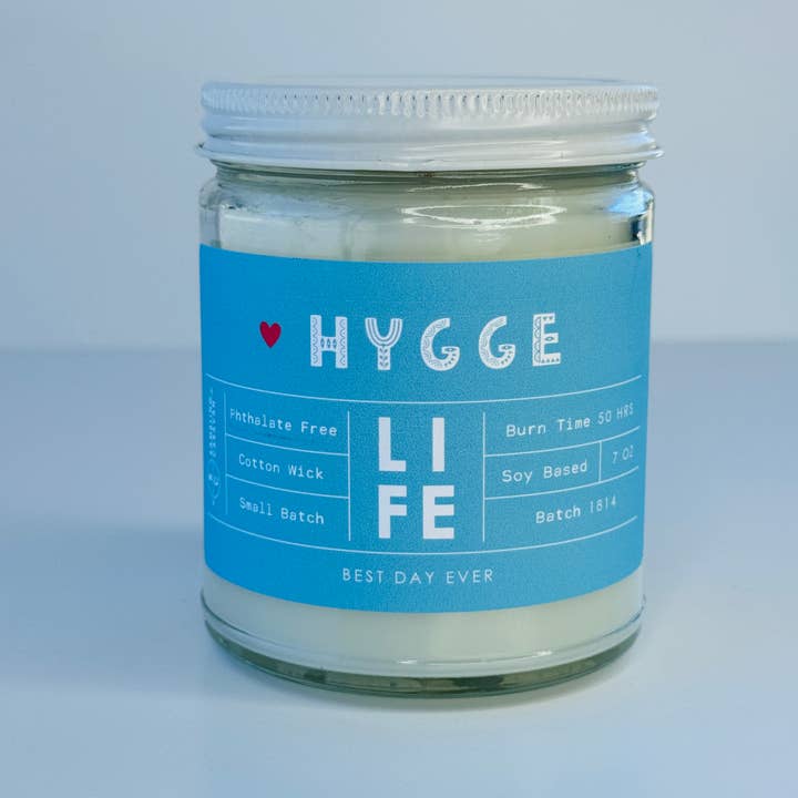 Introducing the Hygge Life Candle, Sea Salt & Orchid Scent, crafted with a soy/coconut-based wax blend for a clean and phthalate-free burn. This candle features a cotton wick and provides up to 50 hours of soothing fragrance. Weighing 7 oz, it is part of Small Batch 1814, featuring a distinctive blue label with a small red heart.