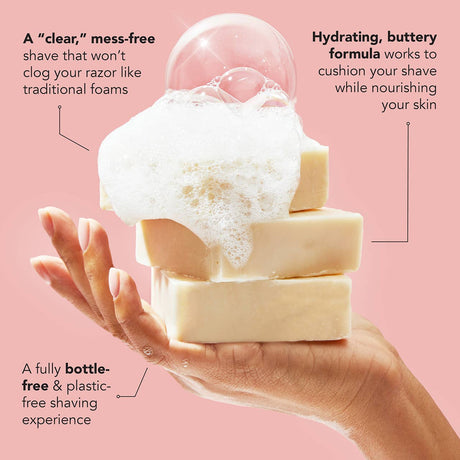 A hand holds four stacked KITSCH Shave Butter Solid Bars, each covered in foam and bubbles, set against a pink background. Text highlights a bottle-free, hydrating, and mess-free shaving experience with the Soap: Shave Butter Solid Bar 4 oz by Kitsch—an innovative alternative to traditional natural shaving cream or vegan shave butter.