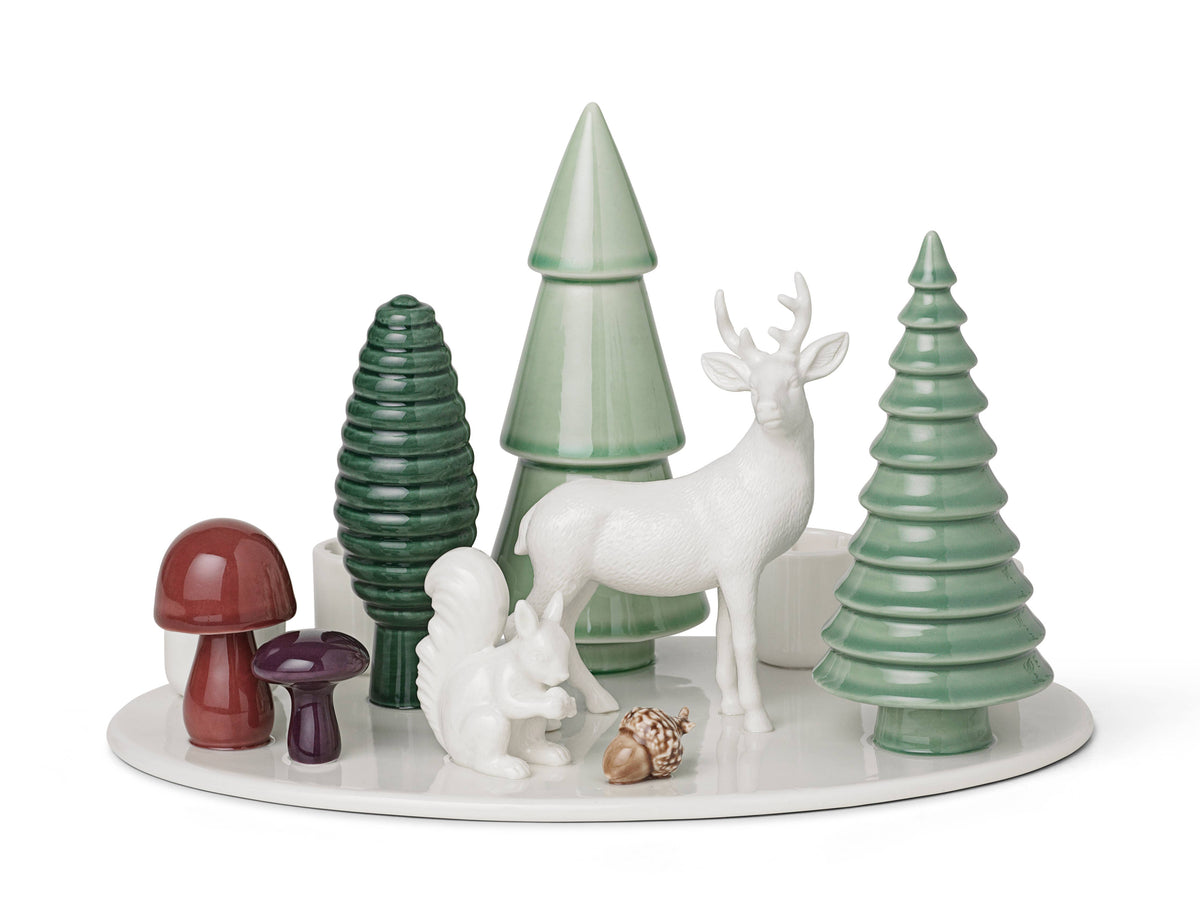 Porcelain advent candle holder on a circular white base, featuring a white deer, squirrel, three green stylized trees, two mushrooms, and an acorn.