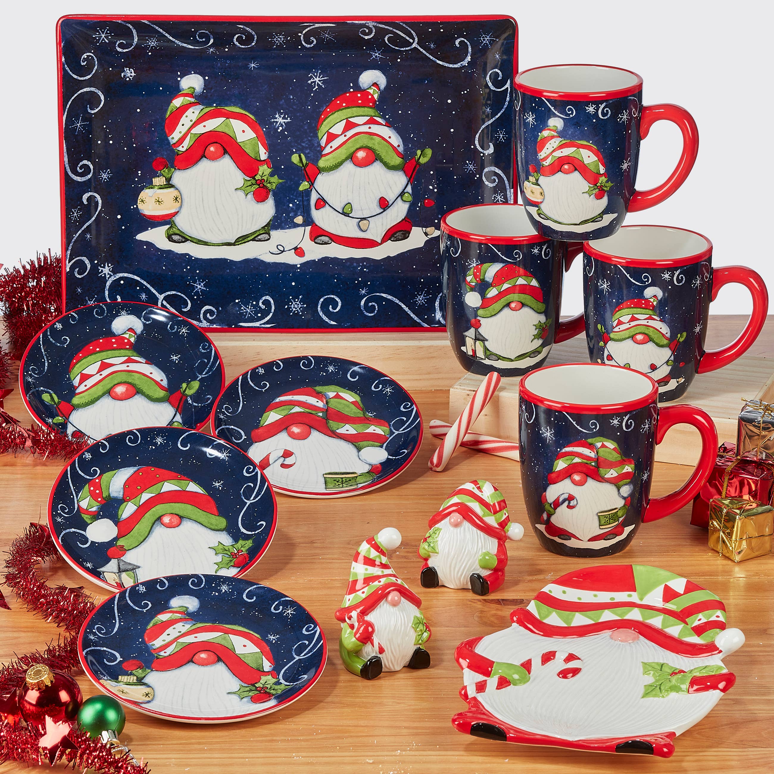 A holiday-themed dinnerware set featuring plates, salt and pepper shakers, and the Holiday Magic Christmas Gnomes Mug 18 oz. (4 variations), all decorated with gnomes in red and green hats on a dark blue background.
