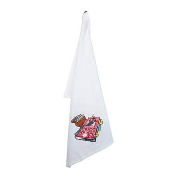 A white Scandinavian tea towel, the "Guide Book Tea Towel Betty Crocker Recipes," hangs on a hook with a small embroidered recipe book design near the bottom corner.