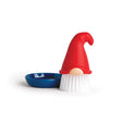 The OTOTO Beardy Tomte Gnome Dish Scrub Brush, 4" tall with a red hat and white bristles, stands beside its 3.25"-diameter blue dish against a white background.