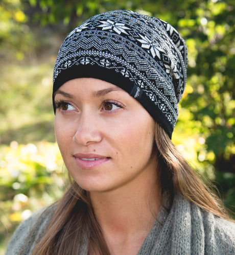 A woman wearing the Northern Story Setesdal Hat in 100% black Merino wool stands outdoors, with green foliage in the background and a textured sweater.