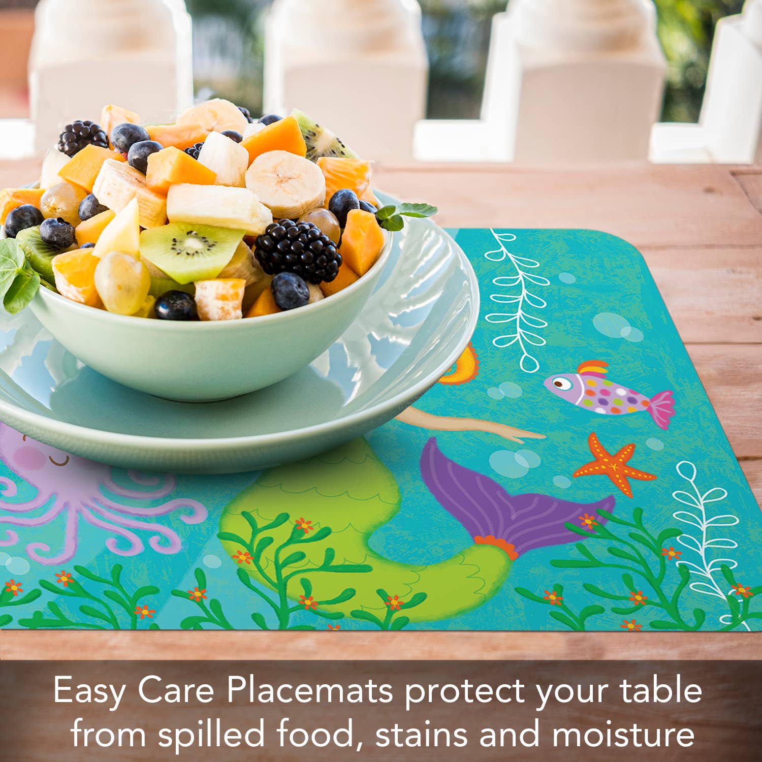 A bowl of mixed fruit rests on a Kids Mermaid Reversible Rectangular Plastic Placemat, designed with an easy-care marine theme and BPA-free for your peace of mind, on a wooden table—an ideal housewarming gift.