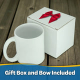 A Mug: Viking Coat of Arms by Odin Limited, featuring a black interior and 11oz ceramic design, is displayed beside a white gift box topped with a red bow on a wooden surface. The text at the bottom reads, "Gift Box and Bow Included.