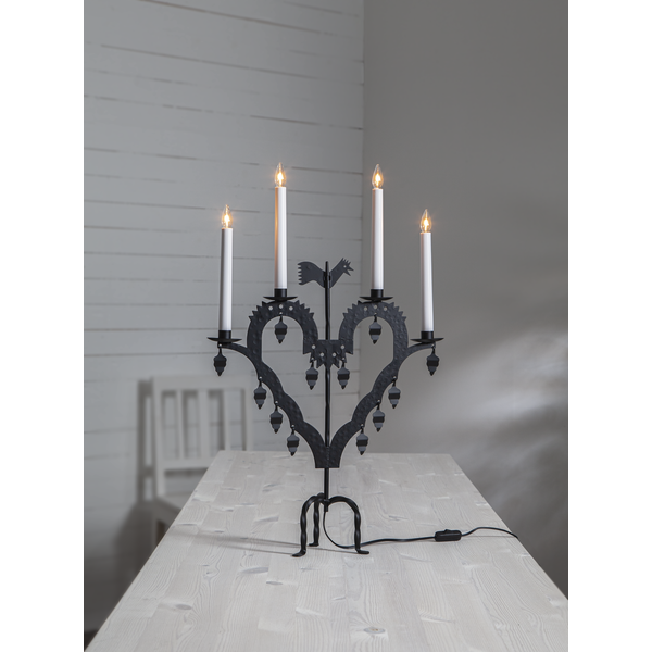 The Star Trading Metal Candlestick El-Tupp, featuring five lit white candles, stands on a light wooden table in a minimal gray room, bringing a subtle Christmas touch.
