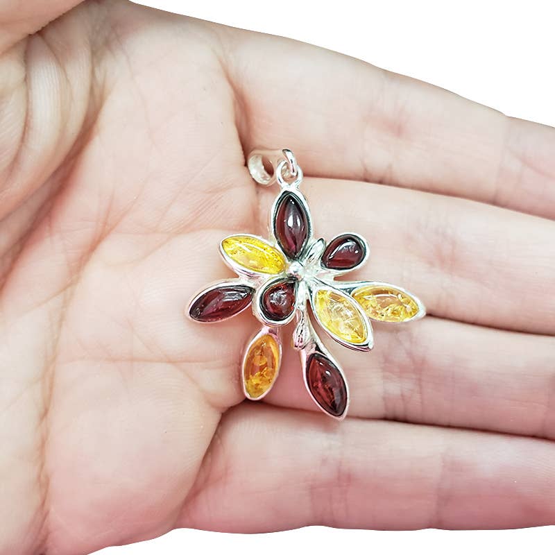A hand holds the Flower Multi Color Amber Silver Pendant, featuring six marquise-shaped Baltic amber stones in warm hues set in sterling silver.