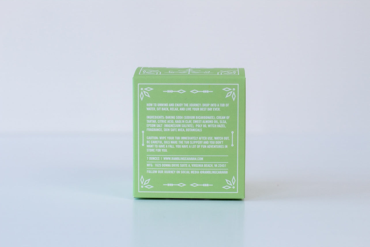 A small green box with white text and decorative borders, displaying Bath Bomb: Coconut Island directions and its skin-nourishing formula on the back, set against a plain white background.