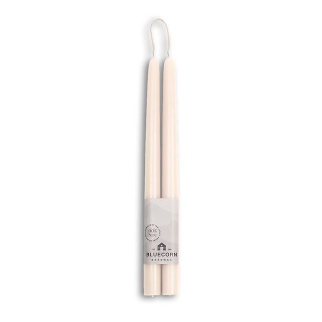 Two 10 eco-friendly, dripless, and handmade white beeswax taper candles are tied together with a Bluecorn Beeswax label featuring a mountain design, stating 100% Pure, ensuring a clean and sustainable burn for any occasion.